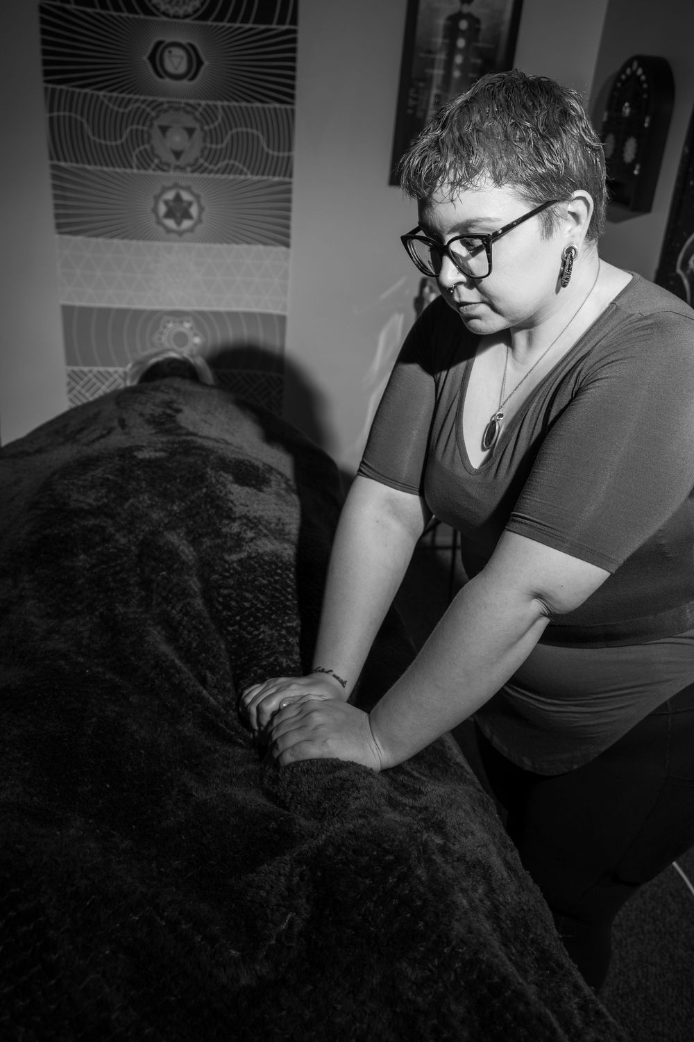 Black and white photo of a woman with glasses performing a massage therapy session on a client covered with a blanket.
