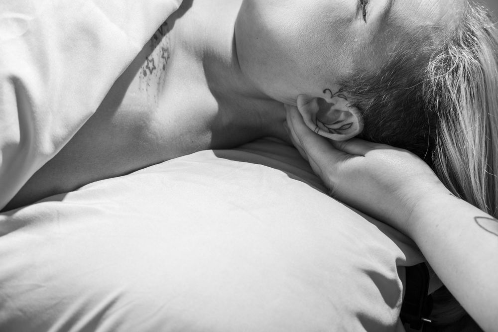 Black and white photo of a person sleeping peacefully on a white pillow with visible tattoos on neck and arm.