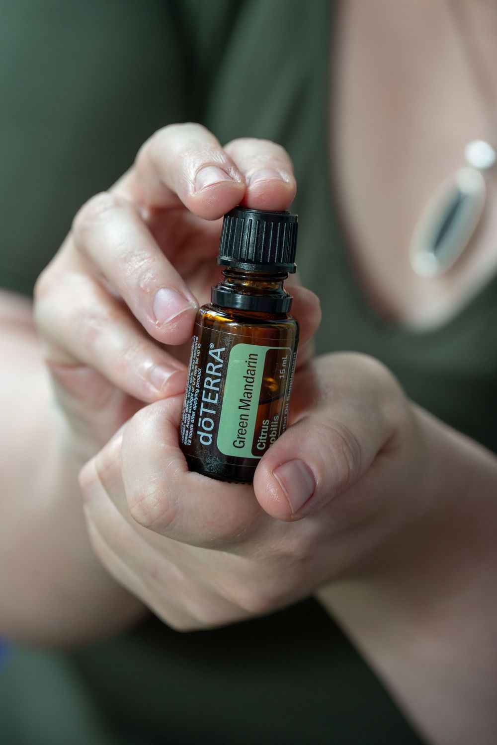Hands holding a small bottle of doTERRA Green Mandarin essential oil, wearing a green shirt.