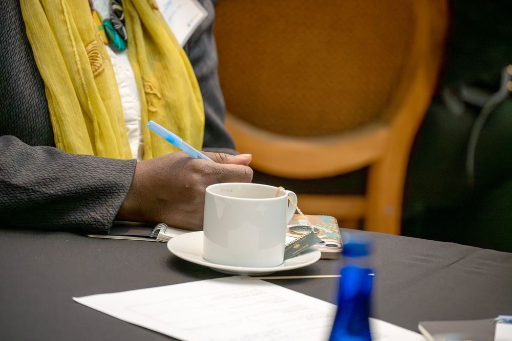 Person in yellow and gray clothing sitting at table with white coffee cup and saucer.