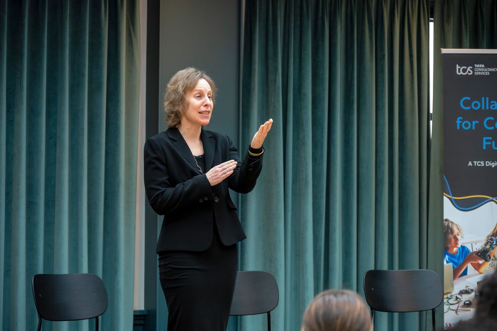 A row of speakers gestures while standing in front of a teal curtain during a business presentation.