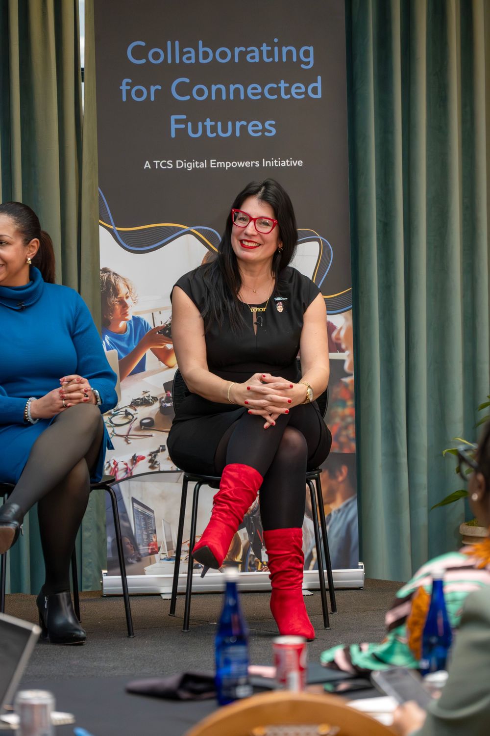 People sit in chairs during a professional collaboration event with signage visible in the background.