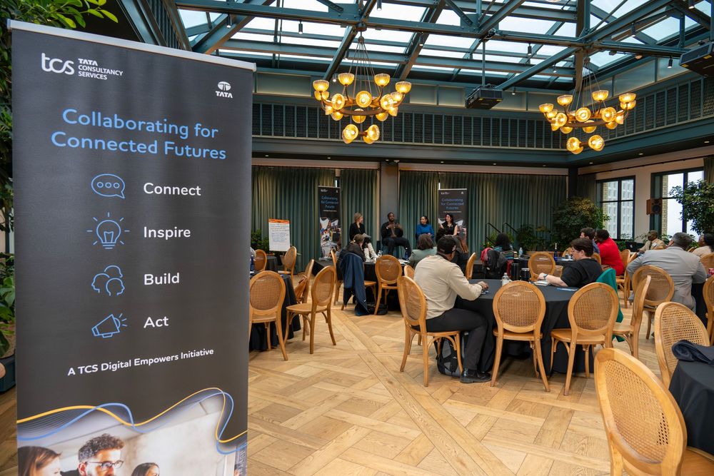 Business conference room with round tables, ornate lighting fixtures and a banner promoting collaborative connected futures.