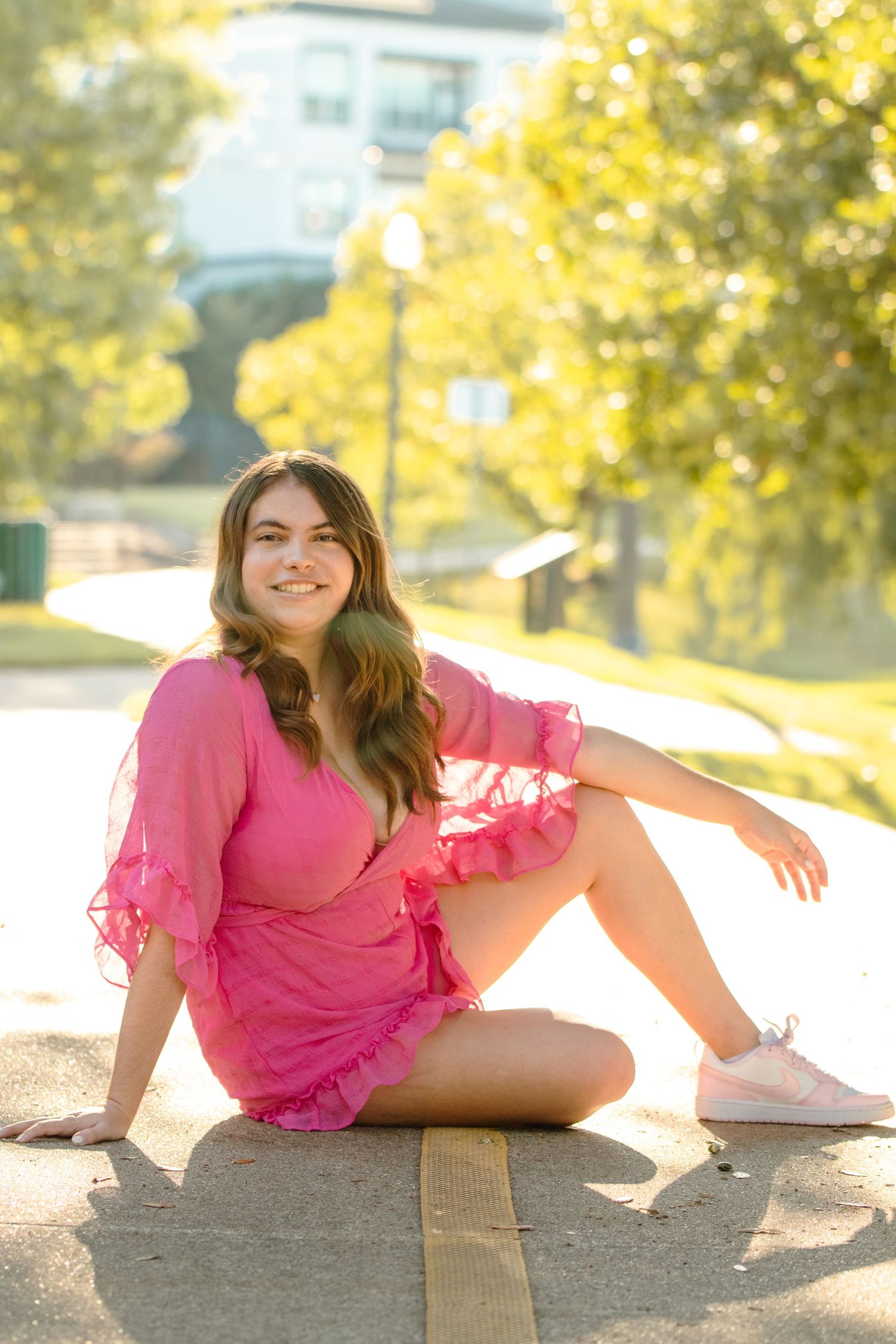 Someone poses in a pink ruffled dress on a sunny path with golden autumn foliage in the background.