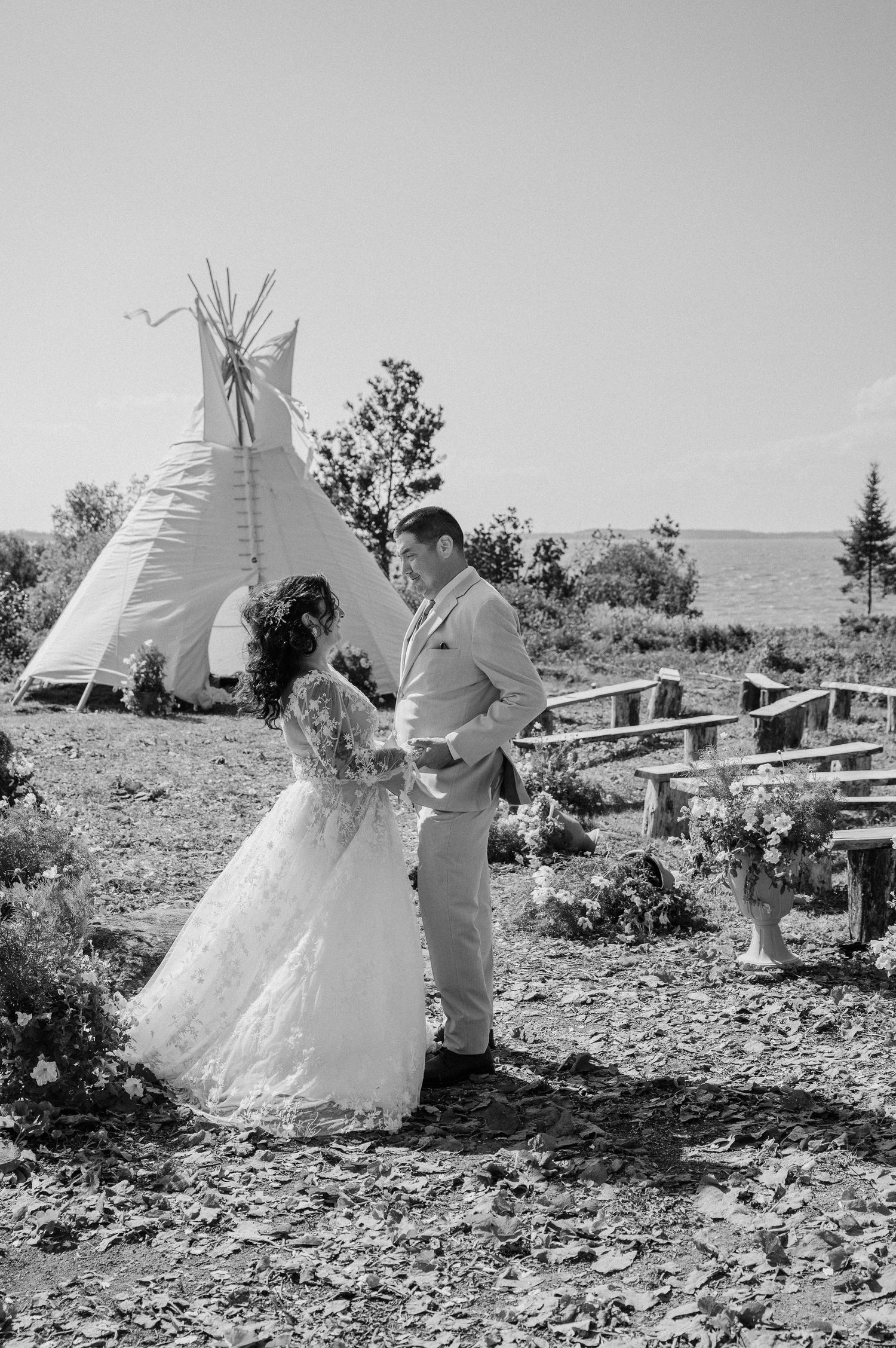 Bride in elegant white dress poses on wooden dock with white tent and lake in background.