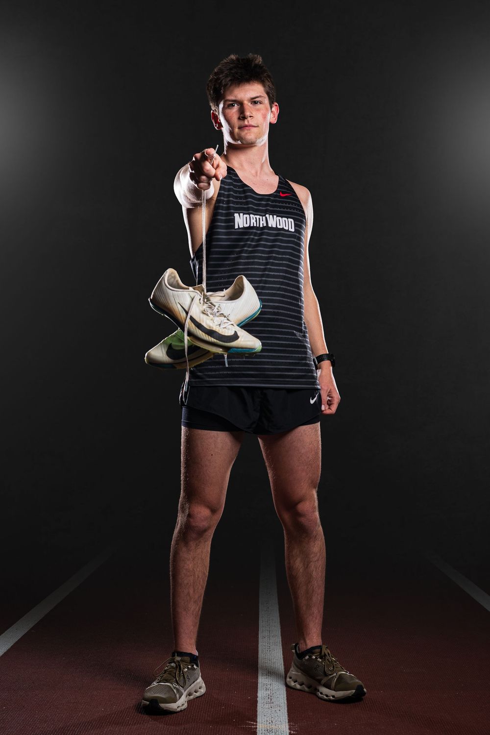 Dynamic Team Media Day Photo of Track athlete holding running shoes while standing on indoor track in dramatic lighting - Nappanee, Indiana