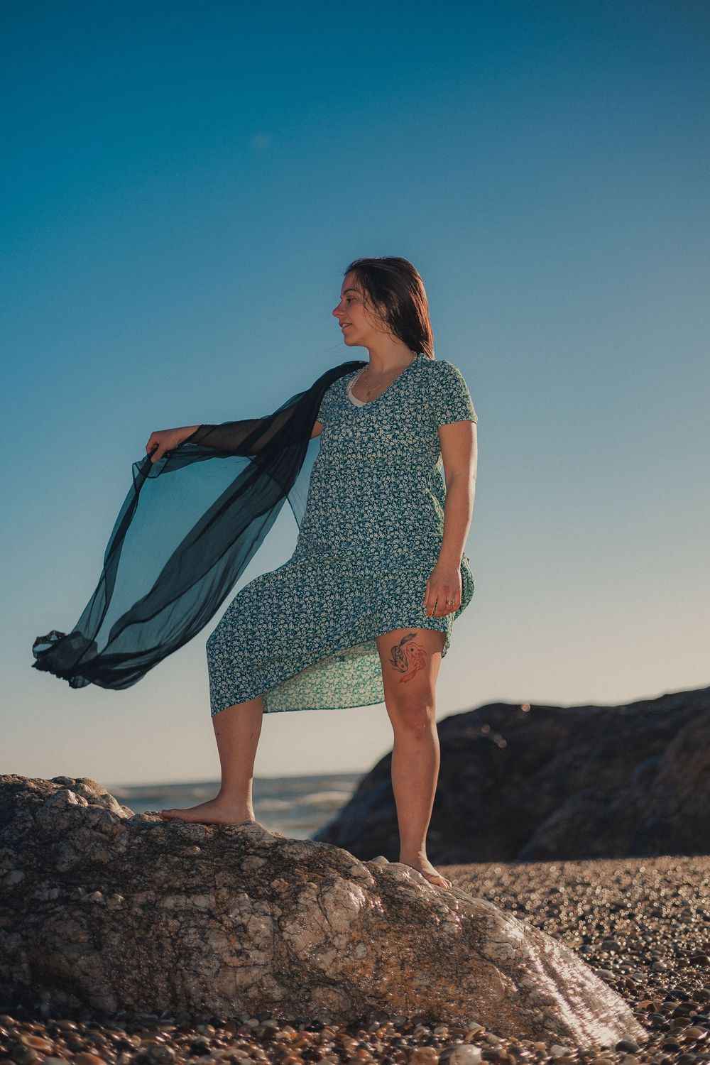 Coastal photoshoot featuring flowing fabric movement against ocean backdrop.