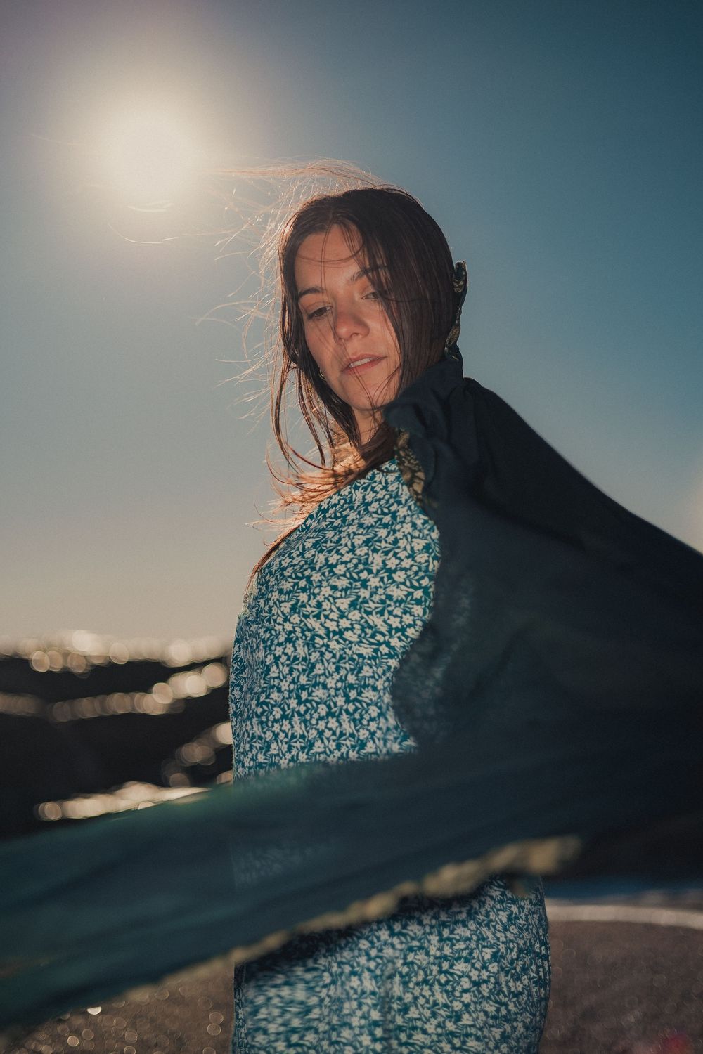 Person in a floral dress poses against a dreamy sunset backdrop on a beach.