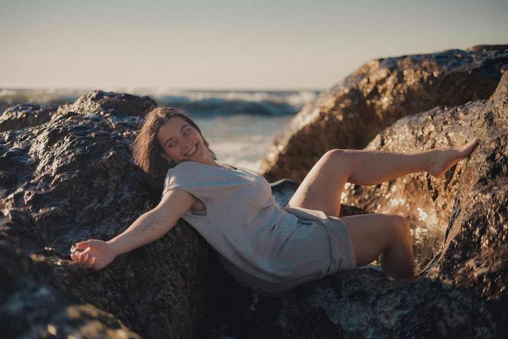 Silhouetted form reclines dramatically on ocean rocks at golden hour.