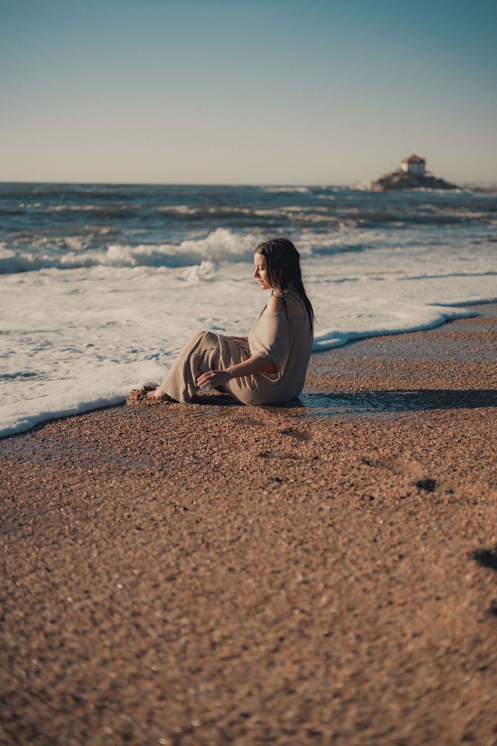 Person relaxes on sandy beach while waves crash in the background.