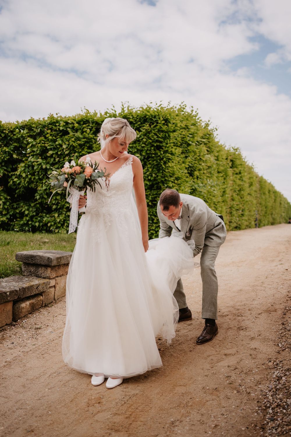 A heartwarming candid sequence of someone helping pick up a dropped bouquet on a dirt path bordered by hedges.
