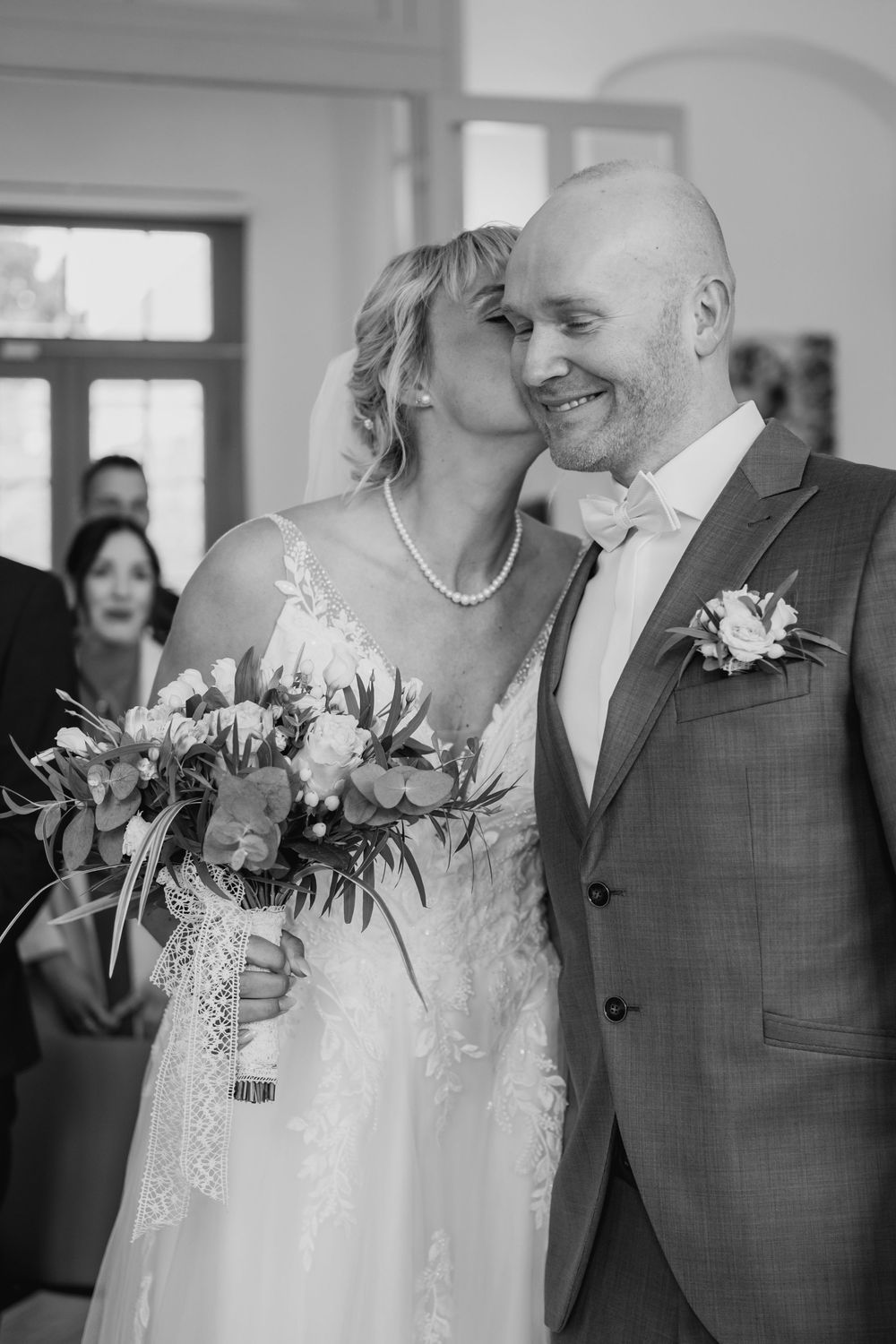 A tender black and white wedding moment with a bride holding a lush bouquet standing close to groom in gray suit.
