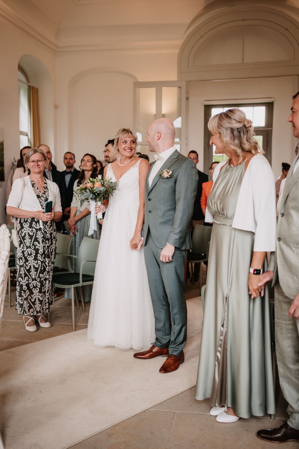 Wedding ceremony in an elegant indoor venue with attendees standing together while wearing formal attire and gowns.