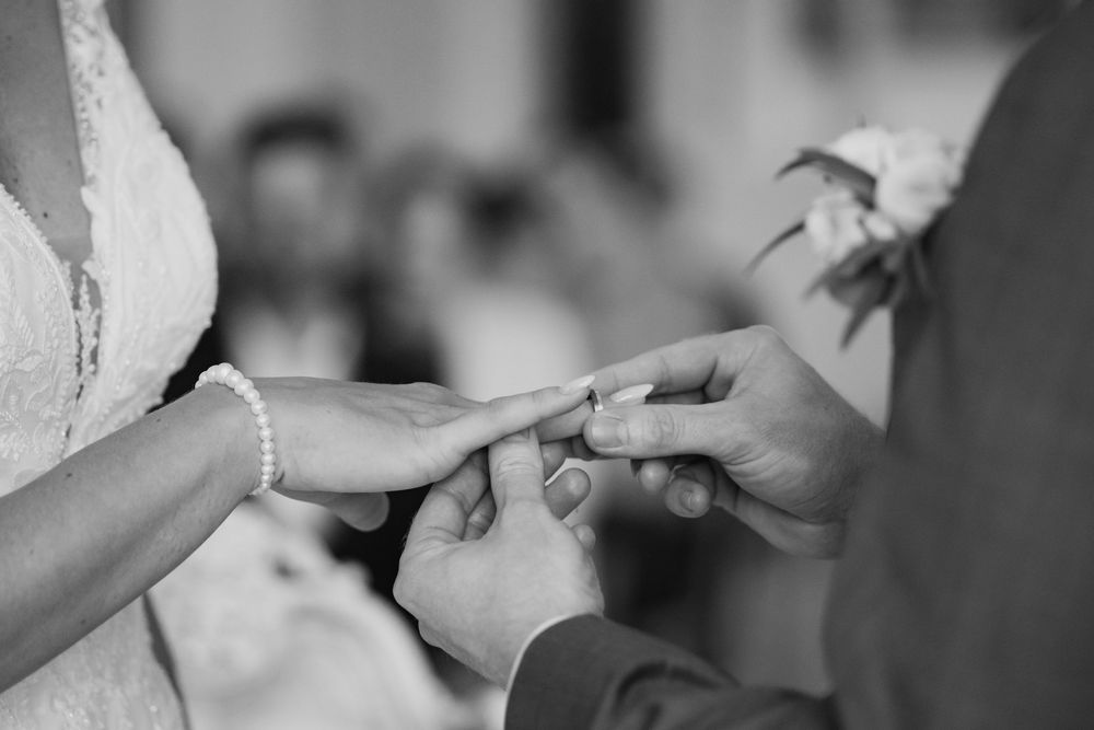 Black and white photo of a ring being placed on a hand during a wedding ceremony.
