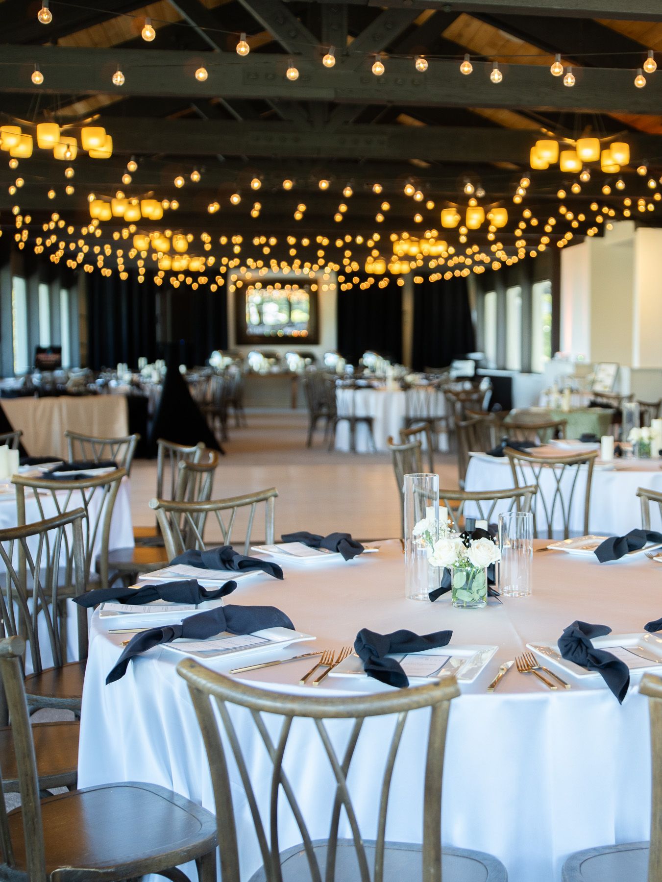 Elegant wedding reception venue with string lights overhead and round tables adorned with navy blue napkins and gold chairs.