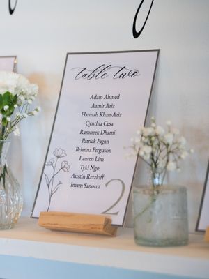 Wedding reception table cards displayed in wooden holders with floral details and elegant calligraphy text.