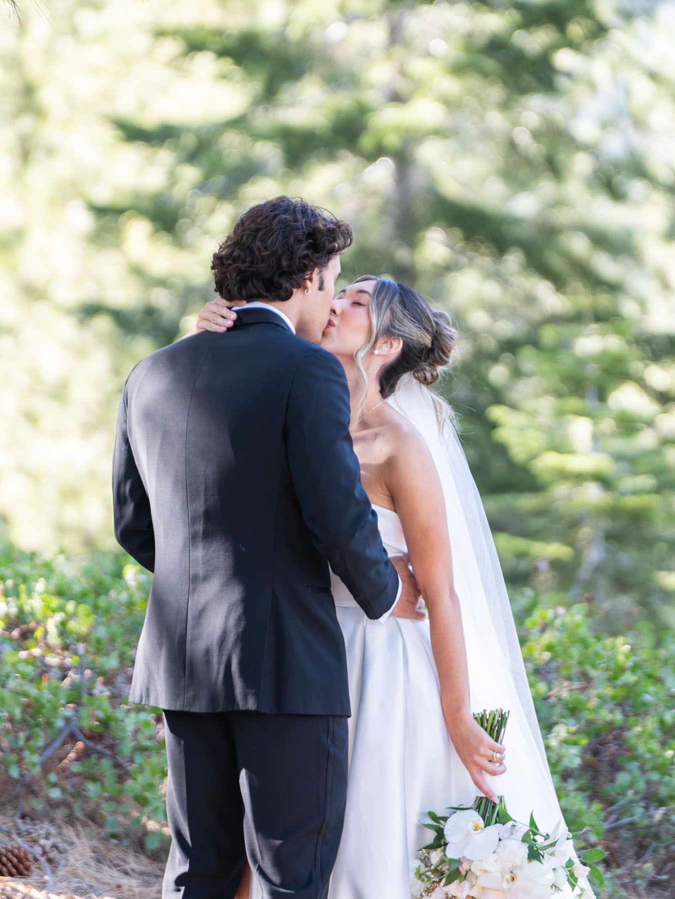 A bride and groom share a romantic kiss during their outdoor woodland wedding ceremony.
