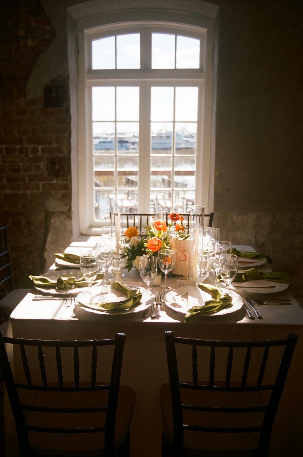 Elegant table settings near arched windows in a rustic brick venue with natural lighting.