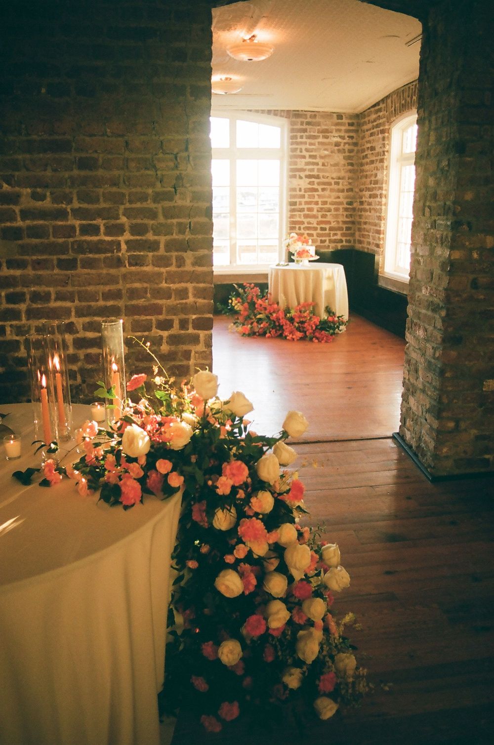 Elegant floral arrangements with pink and peach roses decorate a dimly lit brick-walled venue.