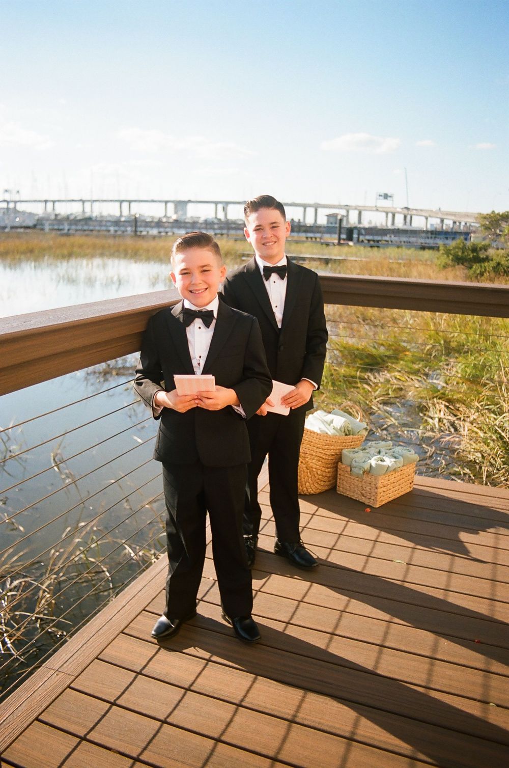 Wedding party members stand on a wooden deck overlooking a waterfront landscape.