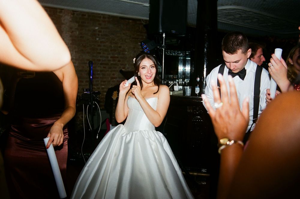 Wedding celebration with dancing guests in formal attire at an indoor reception.