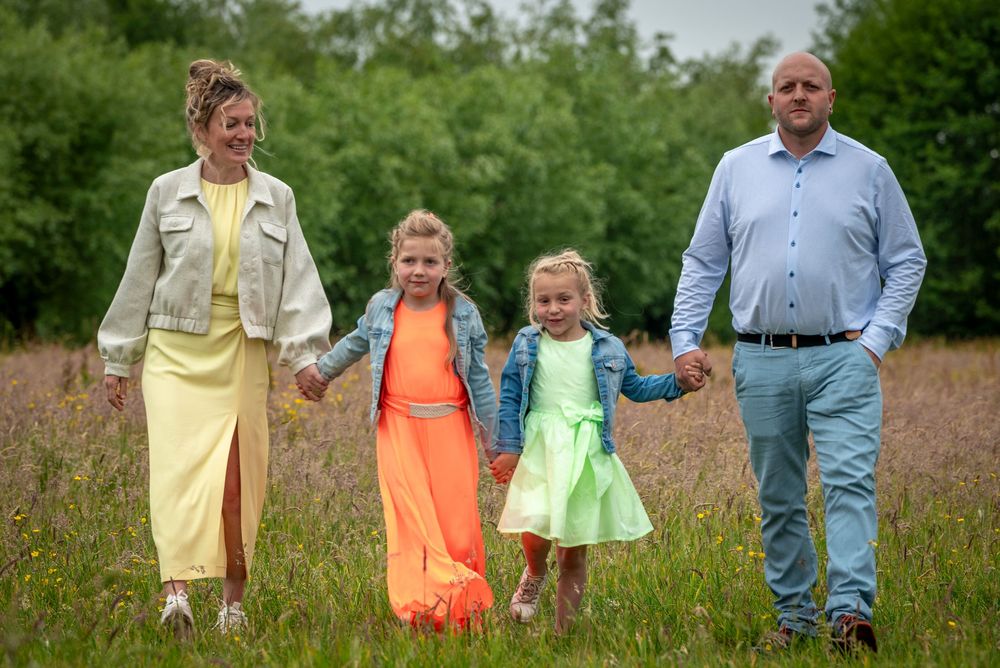 A happy family of four holding hands walking through a wildflower meadow on a cloudy day.