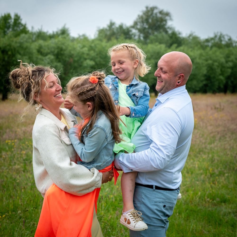 Happy family of four laughing together in a blooming meadow, parents holding their daughters.