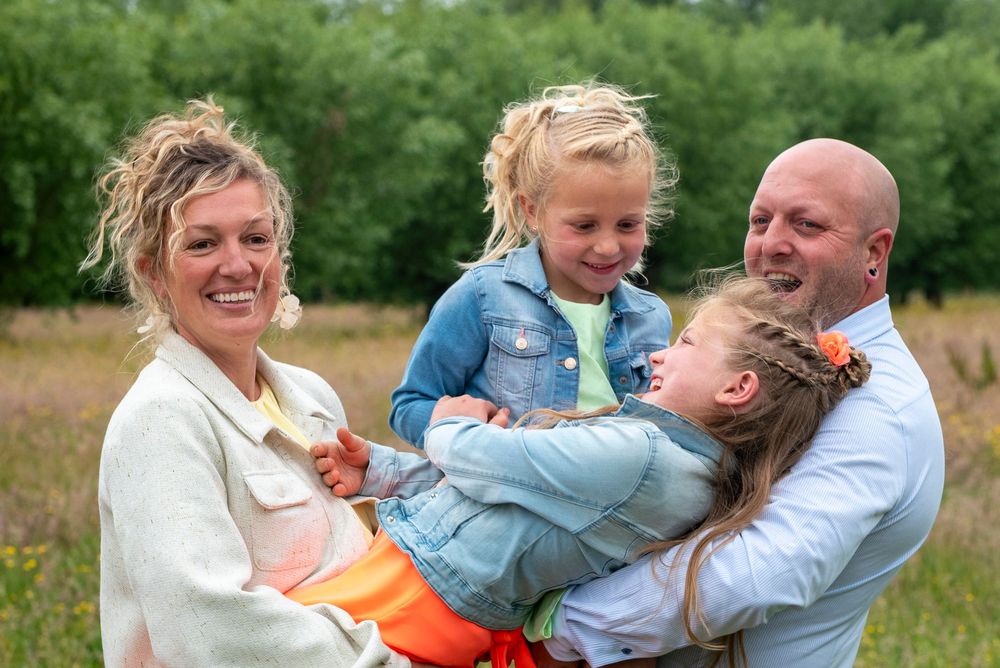 Smiling family of four with two young daughters enjoying a warm outdoor portrait in a green field.