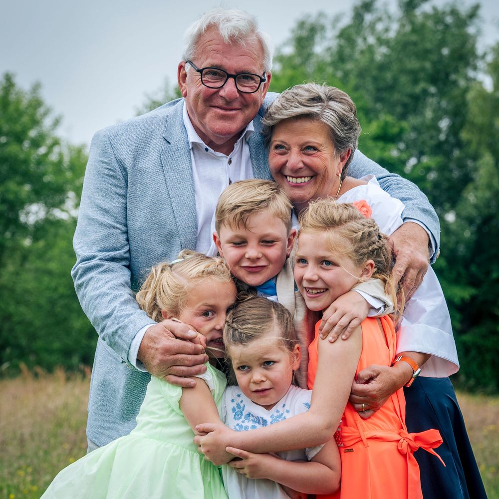 Loving grandparents hugging four grandchildren together in a lush green outdoor setting.
