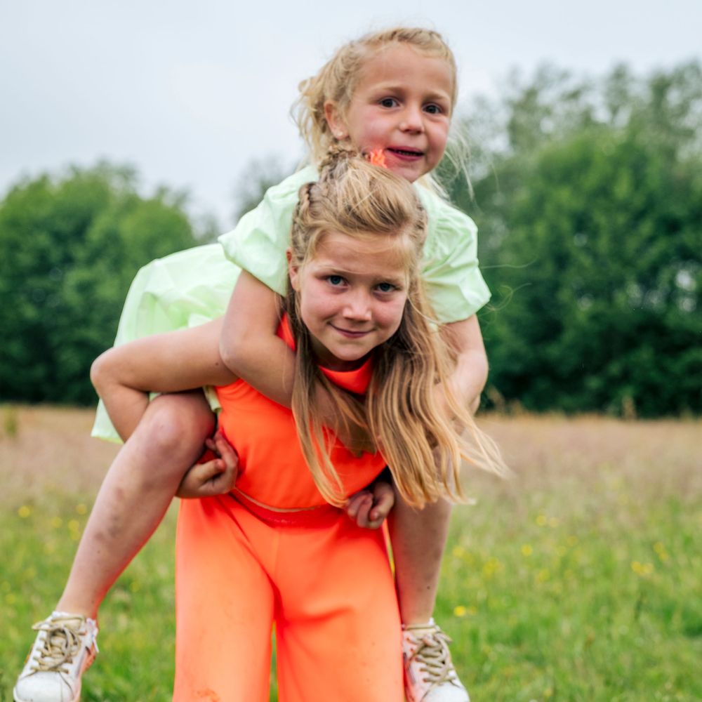 Young girl giving her little sister a piggyback ride in a sunny green meadow.