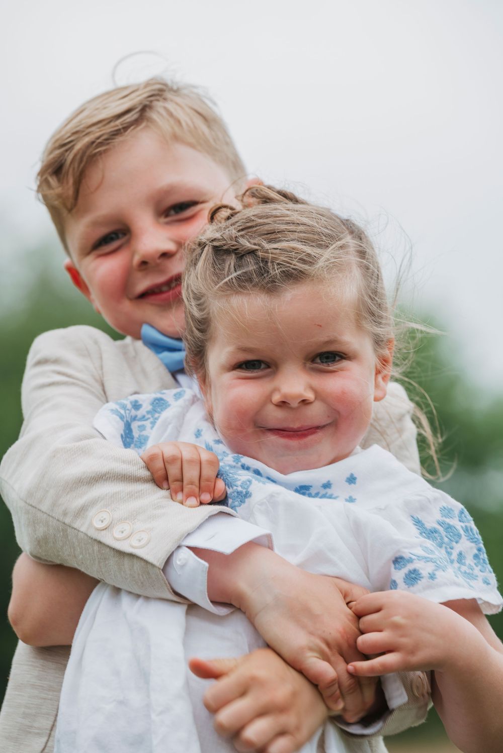 Smiling boy hugging his little sister from behind in a sweet outdoor portrait.