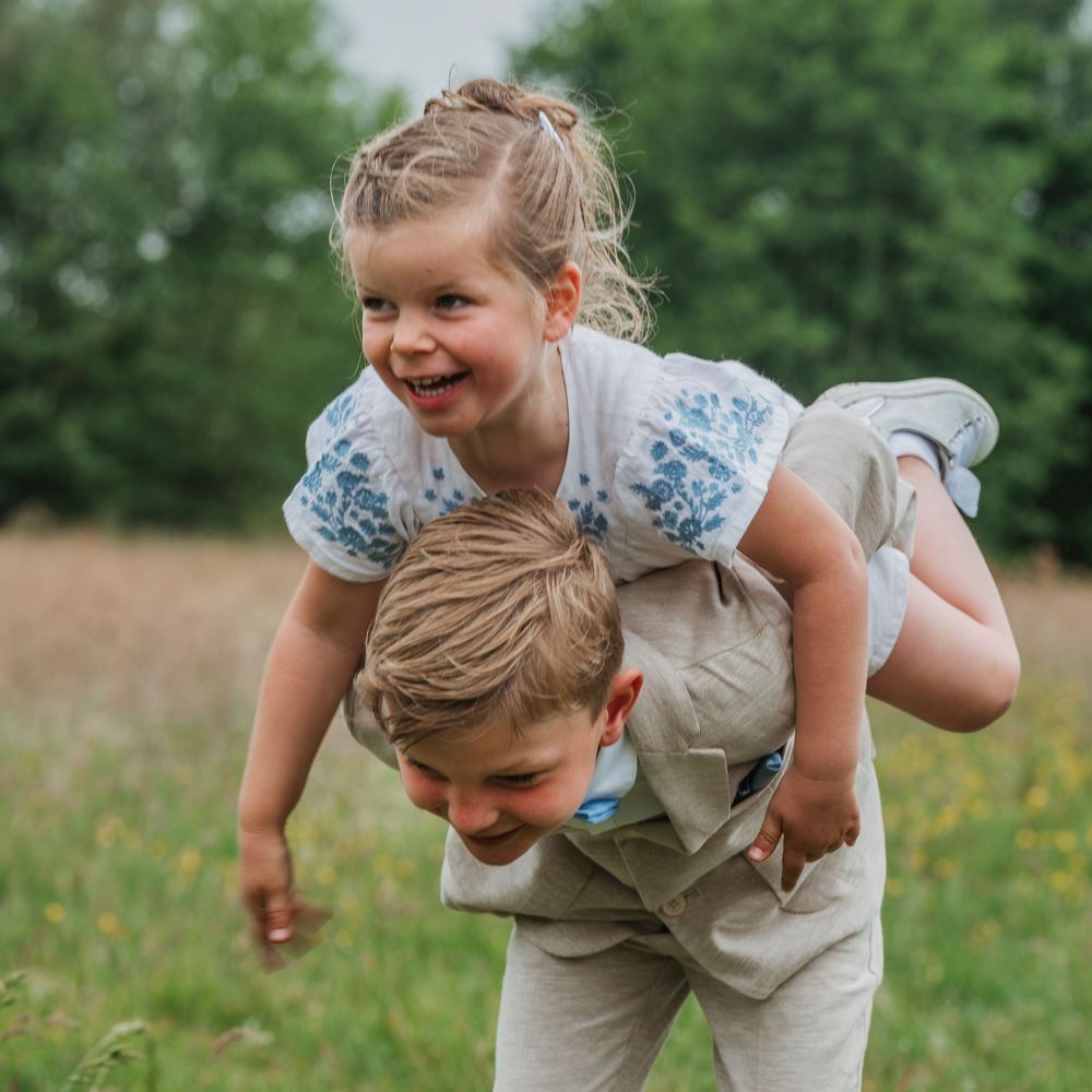 Laughing girl draped over her brother's back as he carries her through a wildflower field.