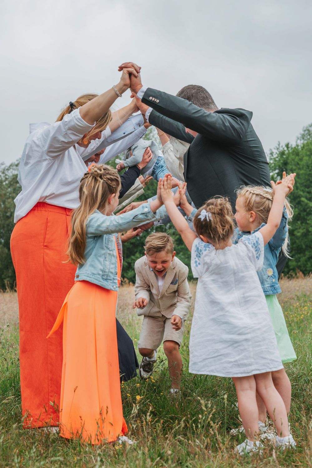 Family celebrating outdoors in a field, raising hands together in a joyful arch over children.