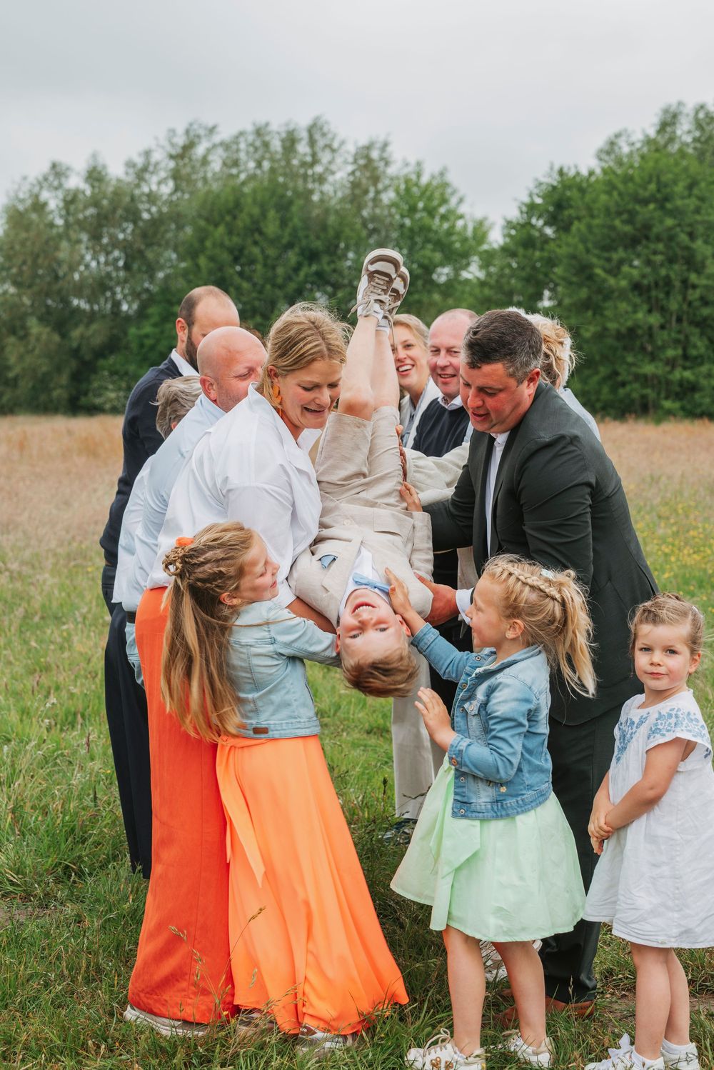 Happy family group lifting a laughing child upside down in a sunny green meadow.