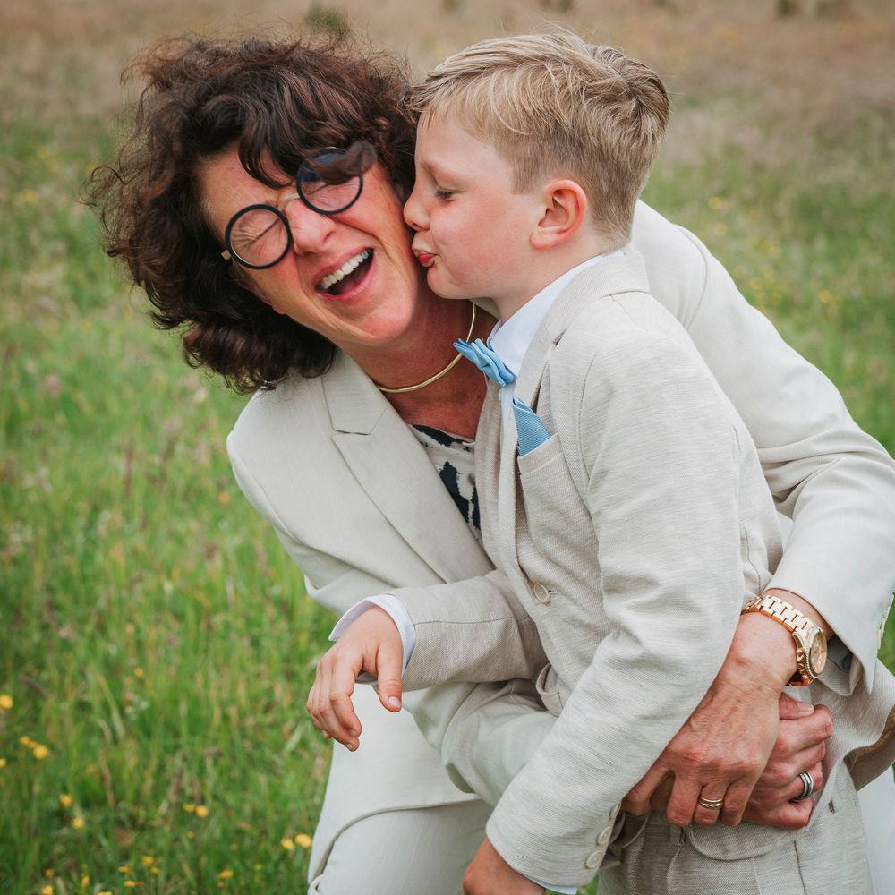 Loving boy gives his laughing grandmother a kiss on the cheek outdoors.