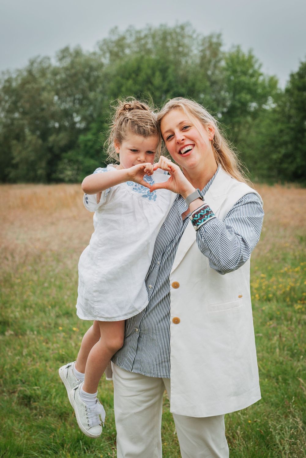 Blonde woman and little girl making heart shapes with their hands in an outdoor field.
