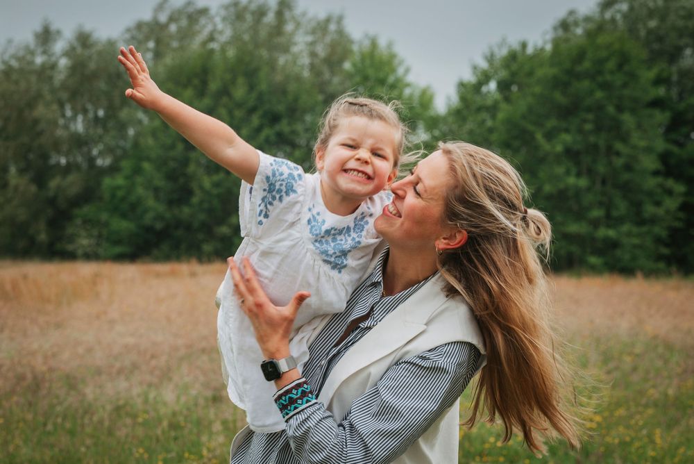 Smiling mother holding her young daughter with arms outstretched in a golden field.