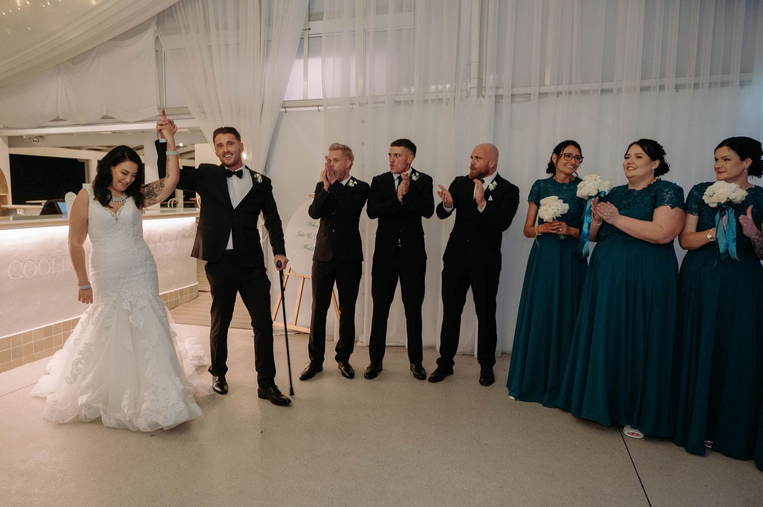 Wedding party poses in formal attire with bridesmaids in teal dresses and groomsmen in black suits.