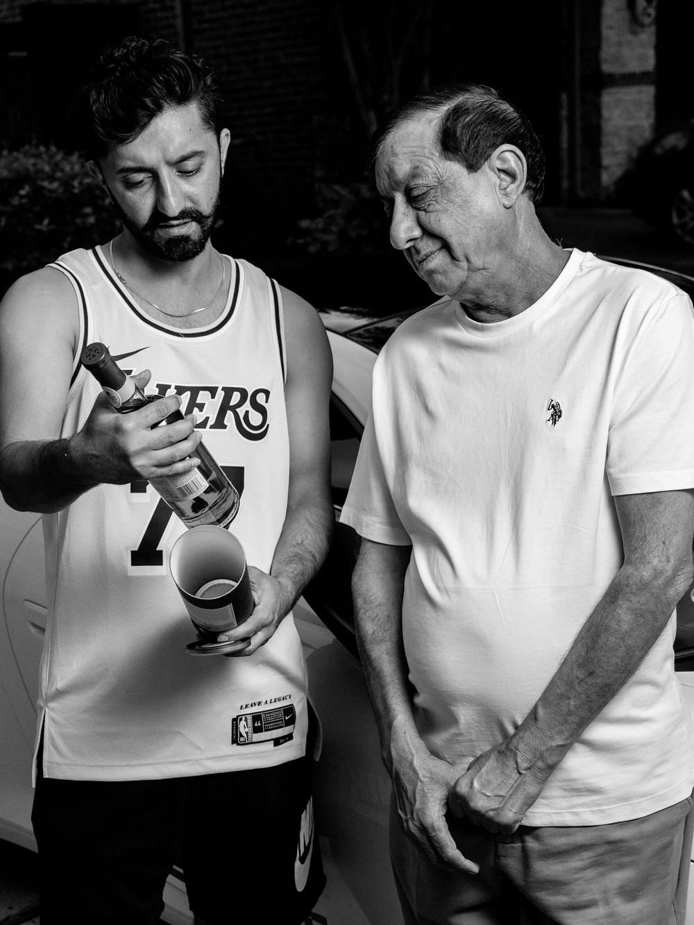 Black and white photo of two people in casual attire looking at something together, one wearing a Lakers jersey.