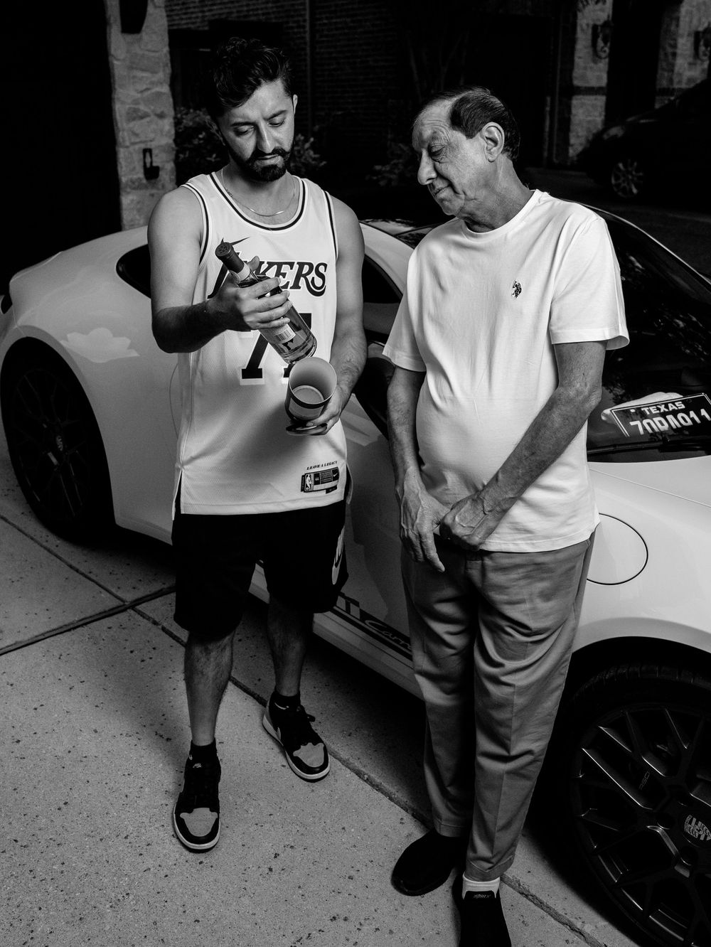 Two figures standing in a monochromatic scene having a conversation near parked cars on the street.