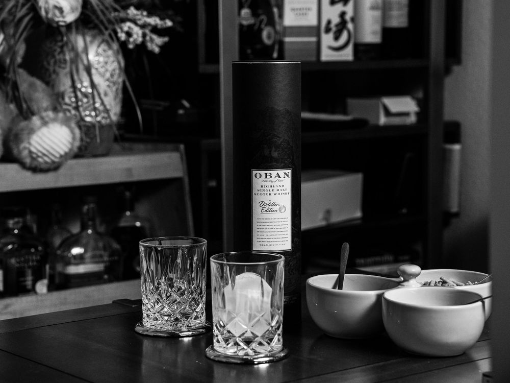 A moody black and white scene of elegant glassware and vintage bottles arranged on a counter or shelf.
