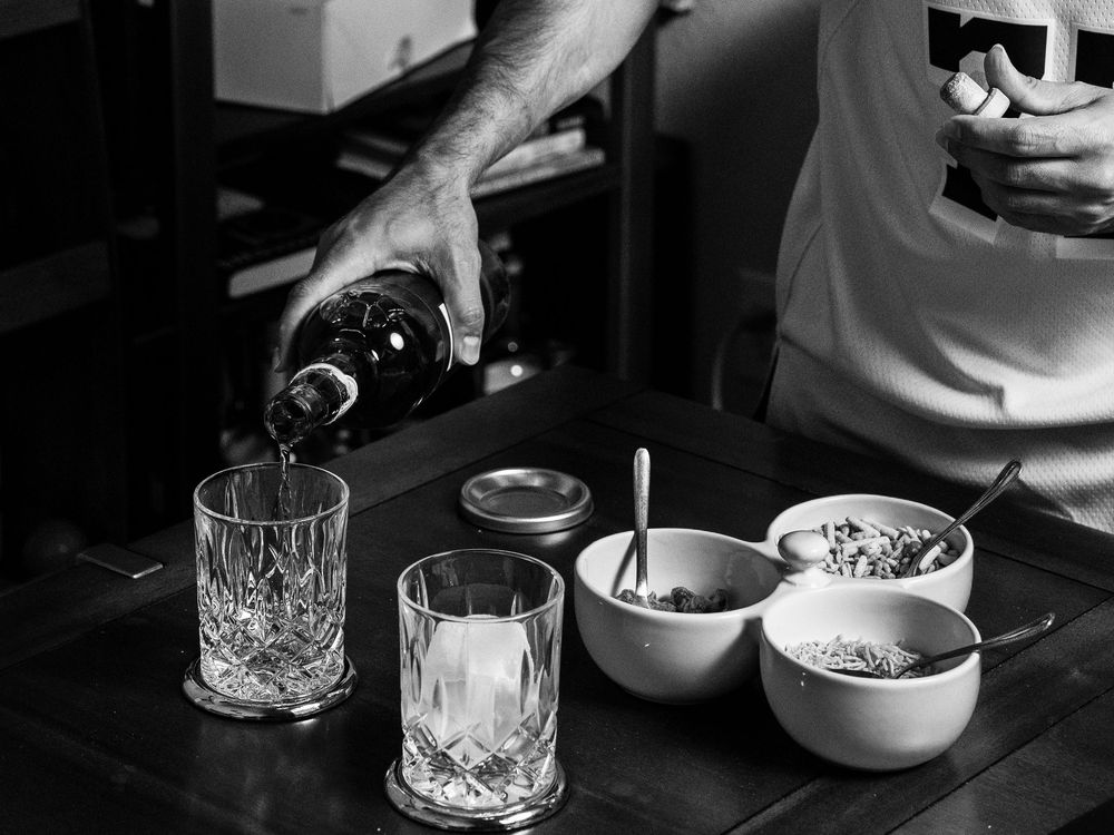 Black and white image of someone pouring drinks at a bar setup with crystal glasses and small bowls of garnishes.