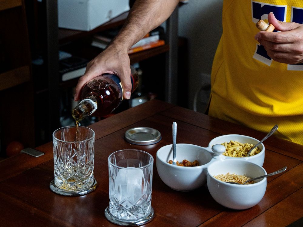 Someone pours whiskey into cut crystal glasses on a wooden table with small bowls of bar snacks.