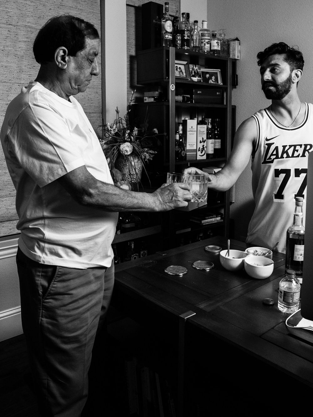 Black and white photo of two people exchanging money across a bar counter in a residential setting.