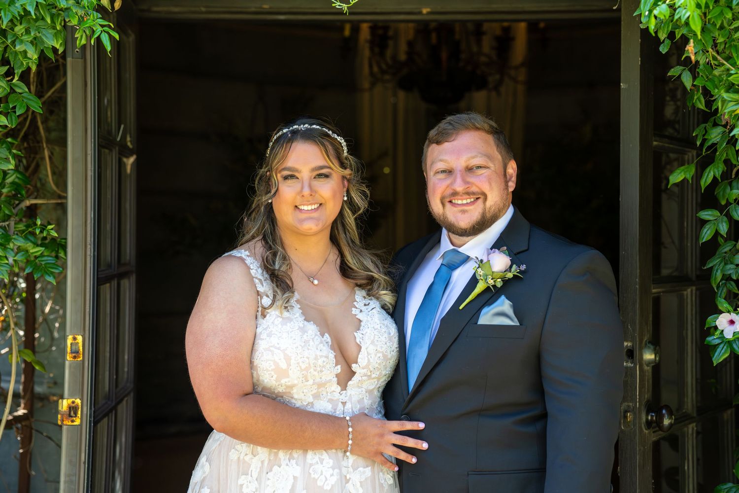 Bride and groom smiling together in wedding attire outside elegant venue doors.