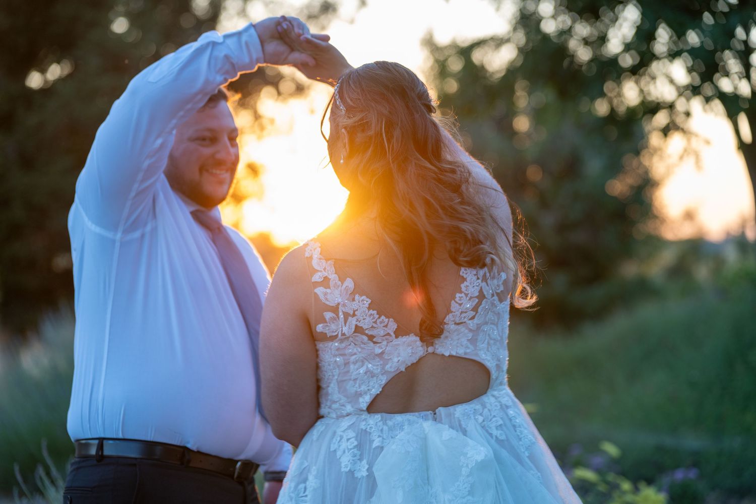 Bride and groom dancing at sunset, golden light glowing behind them, bride in lace backless wedding gown.
