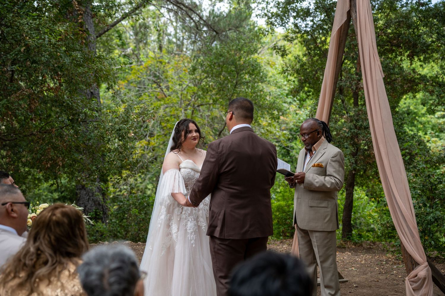 Couple stands at altar during outdoor woodland wedding ceremony with officiant and seated guests.