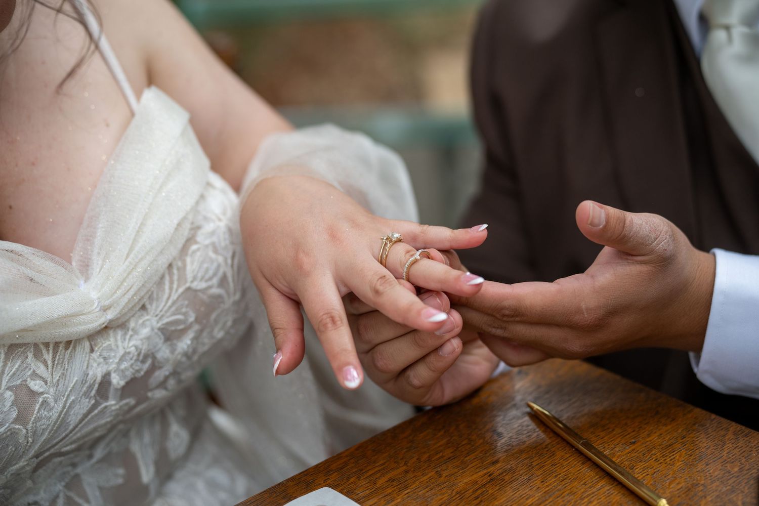 Groom placing a gold wedding ring on bride's finger during wedding ceremony at wooden table.