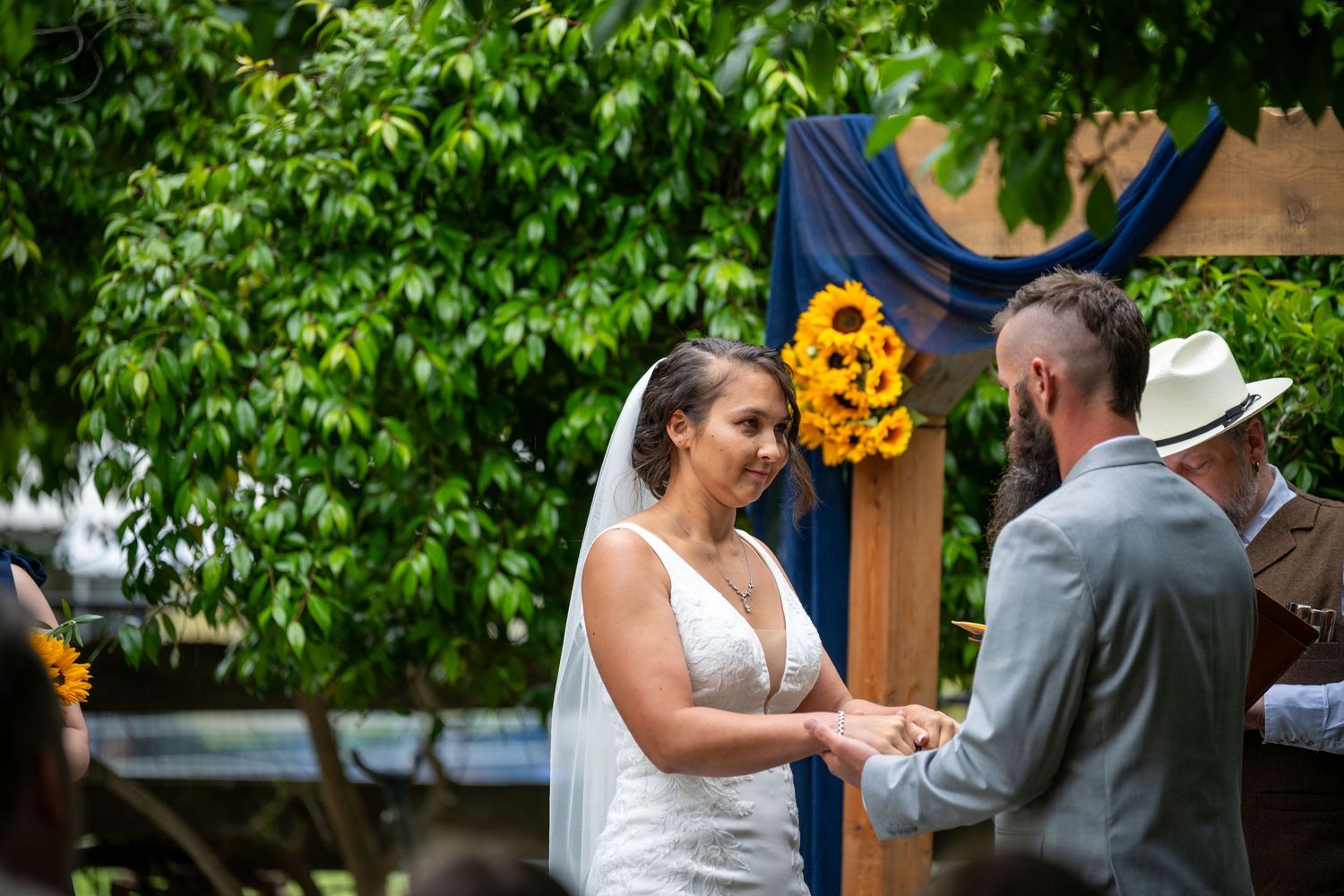 Bride and groom exchange vows outdoors with sunflower arch backdrop and lush greenery during wedding ceremony.