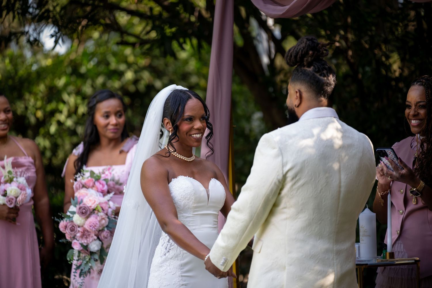 Wedding ceremony in garden setting with pink floral decorations and white formal attire.